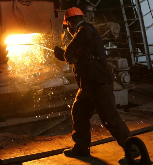 A worker in protective gear welds metal in an industrial plant with sparks flying.