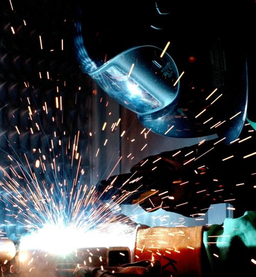 A focused welder works with metal in an industrial setting, creating vibrant sparks.